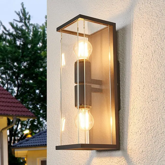 Lucande Außenwandleuchte Annalea - schwarz, klar / transparent, IP54 - Rechteckige Außenwandleuchte mit dunklem Metallrahmen, Klarglasplatten und zwei sichtbaren Glühbirnen, an einer strukturierten Außenwand montiert.