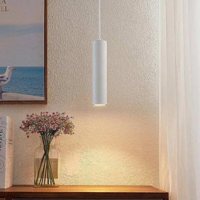 Prios Pendelleuchte Neliyah - weiß / opal, sandweiß, GU10 - Weiße zylindrische Pendelleuchte hängt von der Decke und wirft warmes Licht auf eine Holzfläche mit Blumen.