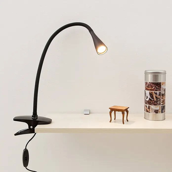 Lindby Klemmleuchte Baris - Farbe Gehäuse: schwarz - Schwarze Klemmleuchte mit flexiblem Arm, beleuchtet ein helles Holzregal. Die Lampe strahlt ein warmes Licht ab.