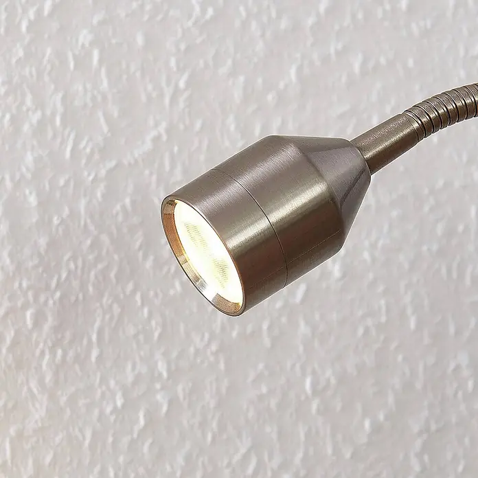 Lindby Klemmleuchte Djamila - L x B x H: 23 x 4 x 39 cm, Farbe Gehäuse: alu / grau / zink - Gebürstete Metall-Schwanenhalslampe mit hellem Licht, die eine strukturierte Wand beleuchtet.