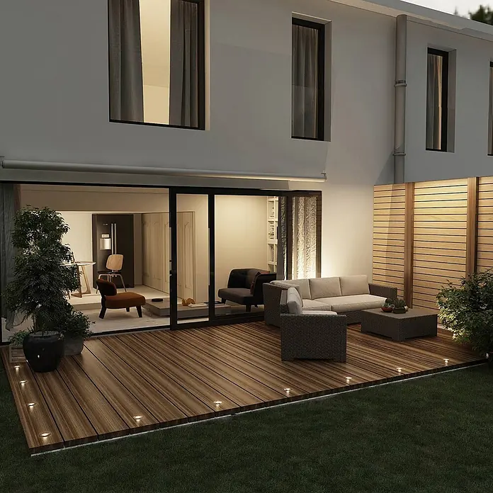 Lindby LED-Gartenstrahler Gracelle - 3.000 K - Kleine, runde LED-Einbauleuchten erhellen nachts den Rand einer modernen Holzterrasse und schaffen eine einladende Atmosphäre.