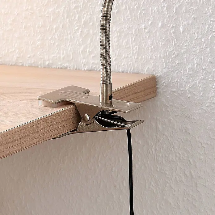 Lindby Klemmleuchte Djamila - L x B x H: 23 x 4 x 39 cm, Farbe Gehäuse: alu / grau / zink - Metall-Klemme für Lampe mit flexiblem Schwanenhals, an ein helles Holzregal geklemmt. Schwarzes Kabel hängt herab.