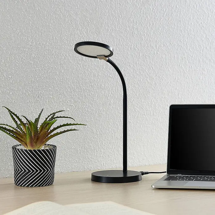Lindby Tischleuchte Binera - schwarz, schwarz - Schwarze Schreibtischlampe mit flexiblem Hals und rundem LED-Kopf, auf einem Holzschreibtisch neben einem Laptop.