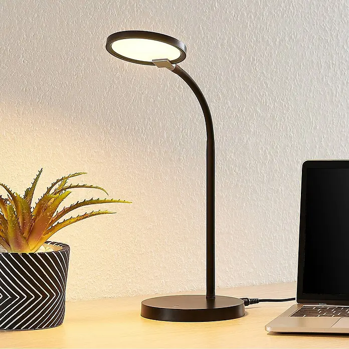 Lindby Tischleuchte Binera - schwarz, schwarz - Schwarze LED-Schreibtischlampe mit flexiblem Arm und rundem Kopf, beleuchtet einen Holzschreibtisch mit Pflanze und Laptop.