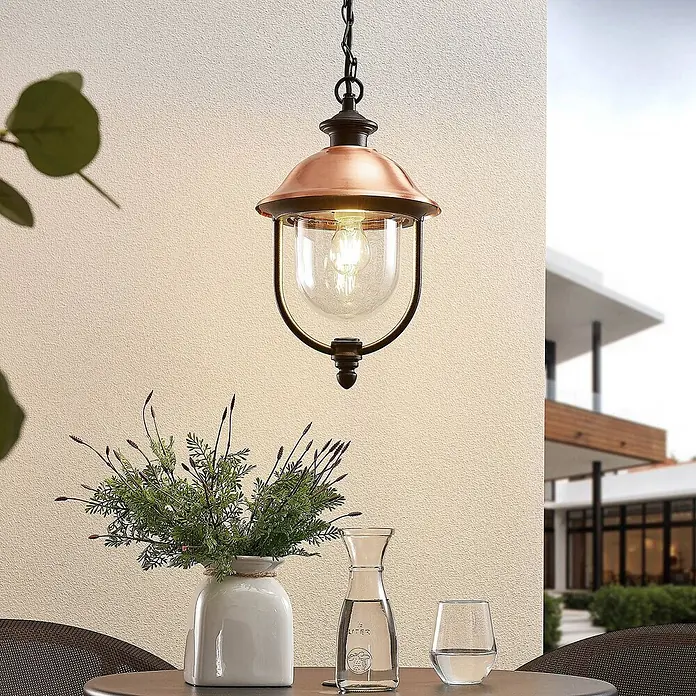 Lindby Außenwand- & Deckenleuchte Clint - kupfer, IP44 - Outdoor-Hängeleuchte mit Kupferschirm und Klarglaskugel über einem Terrassentisch.