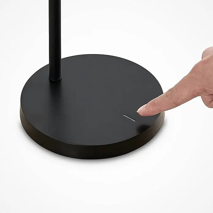 Lindby Tischleuchte Binera - schwarz, schwarz - Ein Finger berührt den beleuchteten Sensor am mattschwarzen Lampenfuß.