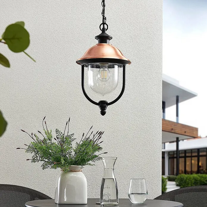 Lindby Außenwand- & Deckenleuchte Clint - kupfer, IP44 - Außen-Pendelleuchte mit Kupferschirm und schwarzem Gestell, über einem Terrassentisch hängend.