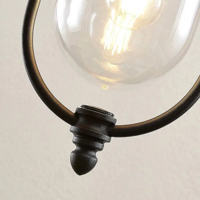 Lindby Außenwand- & Deckenleuchte Clint - kupfer, IP44 - Nahaufnahme einer dunklen, texturierten Metall-Leuchte mit klarer Glasschirm und glühender Glühlampe.