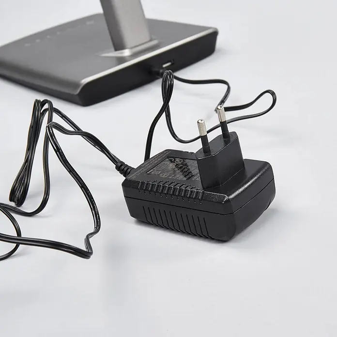 Lindby Tischleuchte Kuno - L x B x H: 37,6 x 15,8 x 46 cm, alu / grau / zink, alu / grau / zink - Schwarzes Netzteil mit zweipoligem EU-Stecker, an ein graues Elektronikgerät angeschlossen.