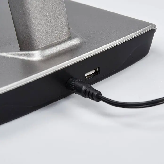 Lindby Tischleuchte Kuno - L x B x H: 37,6 x 15,8 x 46 cm, alu / grau / zink, alu / grau / zink - Grauer Gerätesockel mit schwarzem Netzkabel eingesteckt und freiem USB-Anschluss.