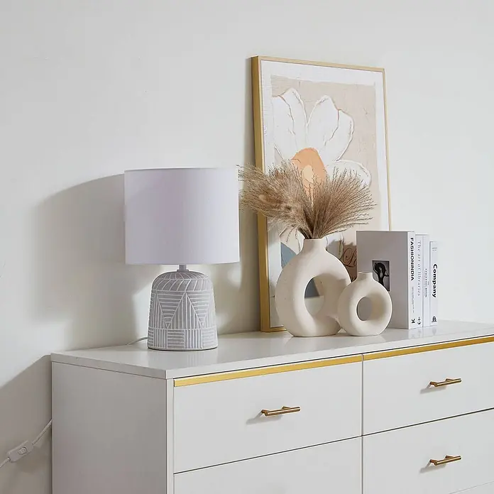 Lindby Tischleuchte Thalassia - L x B x H: 26 x 26 x 40 cm, weiß / opal, weiß / opal, E27 - Weiße Kommode mit goldenen Griffen und Zierleisten, dekoriert mit Lampe, Vasen und Büchern.