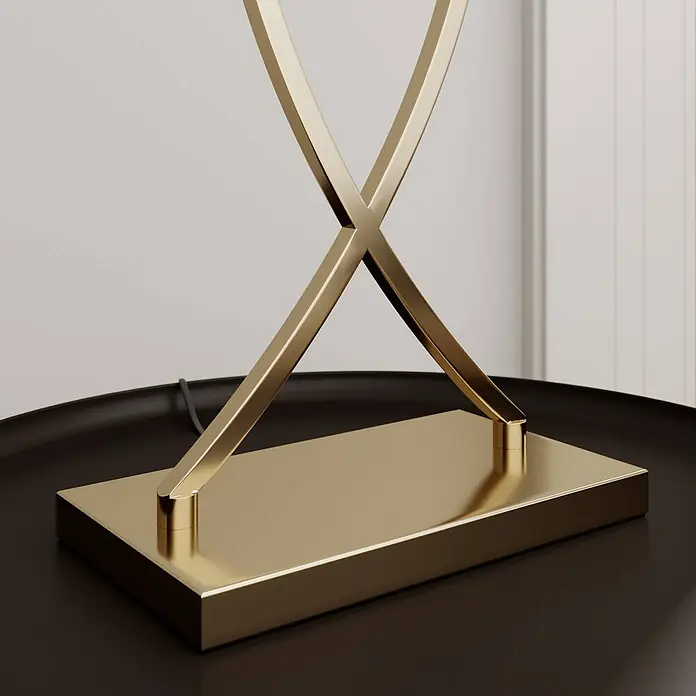 Lucande Tischleuchte Evaine - messing / gold, schwarz, E27 - Goldener Lampenfuß mit X-förmiger Stützstruktur auf einem dunklen Tisch.