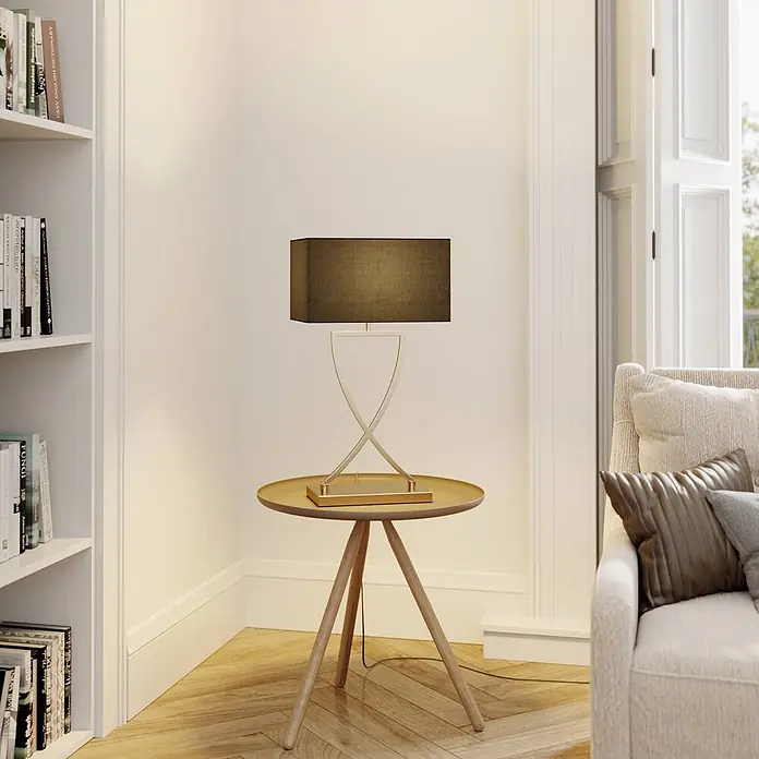Lucande Tischleuchte Evaine - messing / gold, schwarz, E27 - Tischlampe mit rechteckigem, dunklem Stoffschirm und goldfarbenem X-förmigem Metallsockel auf einem runden Holztisch in einem Wohnzimmer.