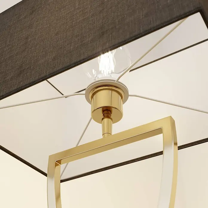 Lucande Tischleuchte Evaine - messing / gold, schwarz, E27 - Nahaufnahme einer Lampe mit schwarzem Stoffschirm, goldenem Metallrahmen und beleuchteter Glühbirne.
