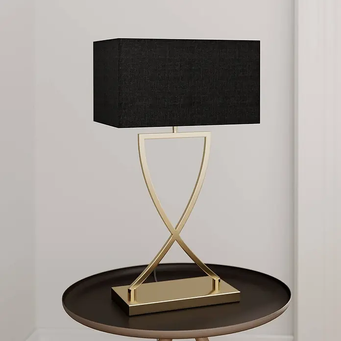 Lucande Tischleuchte Evaine - messing / gold, schwarz, E27 - Moderne Tischlampe mit schwarzem rechteckigem Schirm und goldenem X-förmigem Metallsockel auf dunklem Rundtisch.