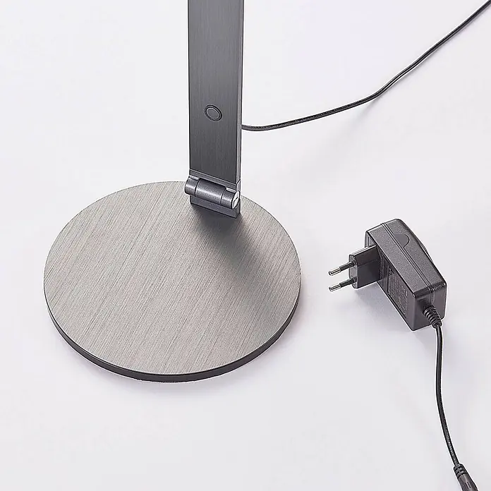 Lucande Tischleuchte Mion - L x B x H: 35 x 18 x 41 cm, alu / grau / zink, alu / grau / zink - Gebürsteter Metall-Schreibtischlampenfuß mit Scharnier und Taste, neben einem schwarzen Netzteil mit europäischem Stecker.