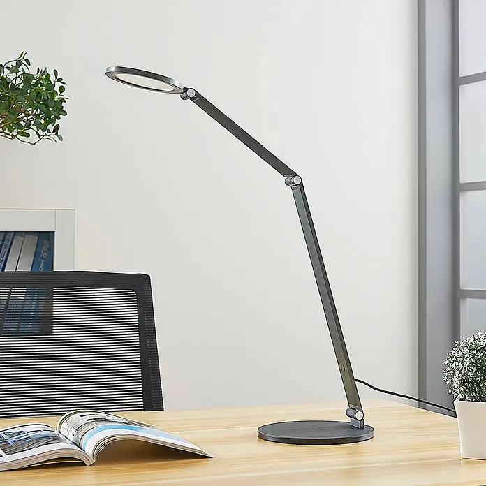Lucande Tischleuchte Mion - L x B x H: 35 x 18 x 41 cm, alu / grau / zink, alu / grau / zink - Elegante dunkelgraue, verstellbare LED-Schreibtischlampe mit rundem Kopf und Fuß auf einem Holzschreibtisch.