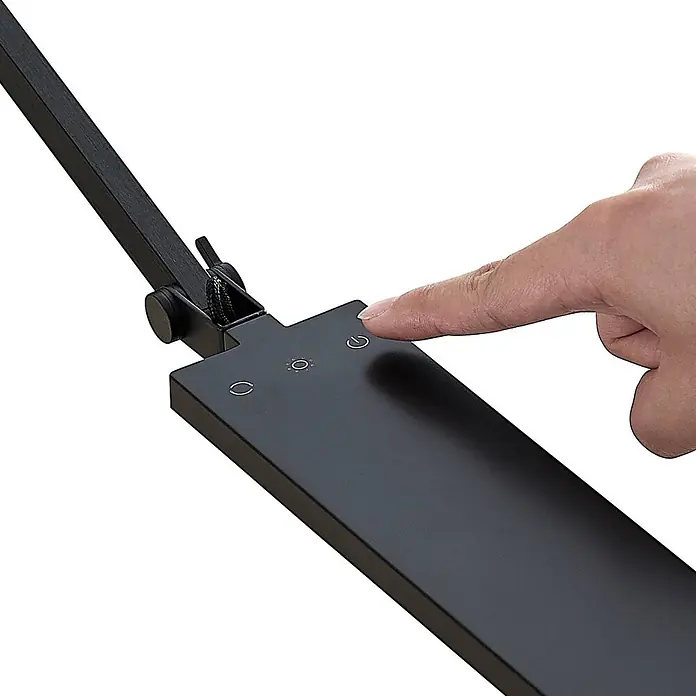 Lindby Tischleuchte Antisa - L x B x H: 65 x 14 x 47 cm, schwarz, schwarz - Finger drückt den Einschaltknopf einer mattschwarzen Schreibtischlampe, die ihr Bedienfeld mit Touch-Symbolen für Leistung, Helligkeit und Modus zeigt.