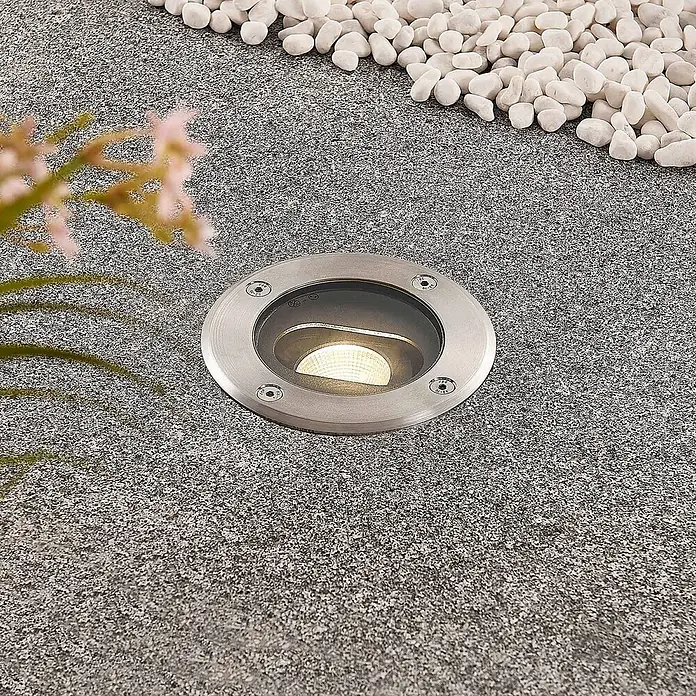 Lucande LED-Gartenstrahler Doris - 3.000 K, 12 x 12 x 15 cm - Runder Bodeneinbaustrahler aus gebürstetem Edelstahl, in gesprenkeltem Graustein eingelassen, beleuchtet einen von weißen Kieselsteinen gesäumten Weg.