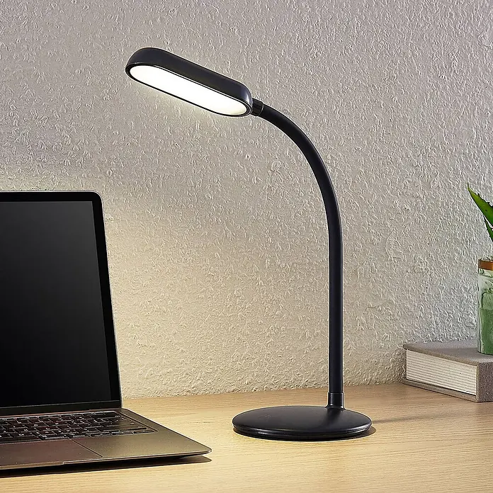 Prios Tischleuchte Opira - schwarz, schwarz - Schwarze flexible LED-Schreibtischlampe mit länglichem Kopf, auf einem Holzschreibtisch neben einem Laptop.