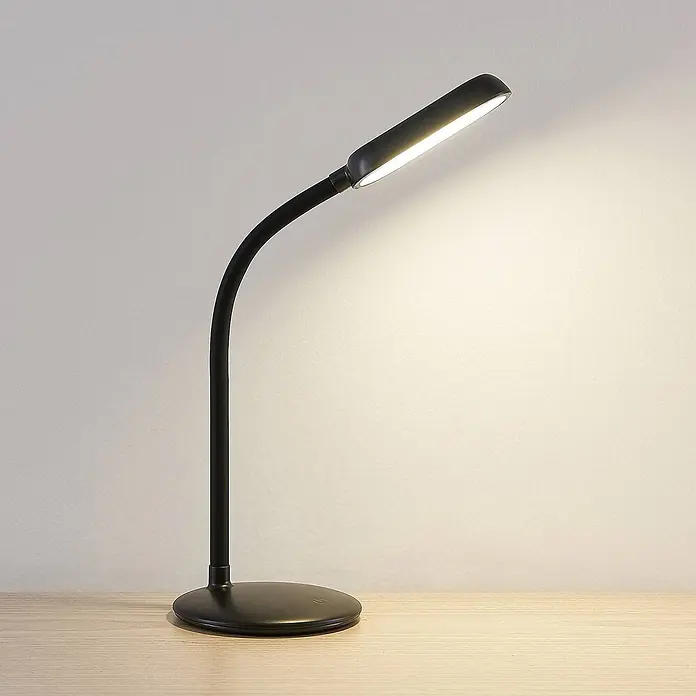 Prios Tischleuchte Opira - schwarz, schwarz - Schwarze Schreibtischlampe mit flexiblem Hals und beleuchtetem linearem Kopf, die auf einem Holztisch leuchtet.