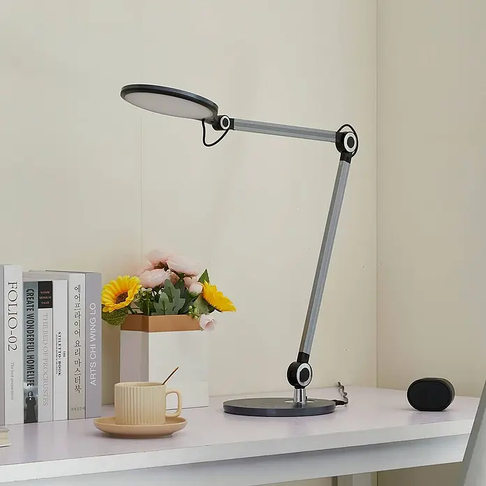 Lindby Tischleuchte Nyxaris - alu / grau / zink, alu / grau / zink - Moderne, verstellbare LED-Schreibtischlampe mit grauem Gelenkarm, rundem Kopf und dunklem Rundfuß auf einem Schreibtisch.