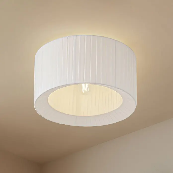 Lindby Deckenlampe in weiß, Deckenleuchte rund -  - Weiße Deckenleuchte aus plissiertem Stoff, beleuchtet, an einer hellbeigen Decke montiert.