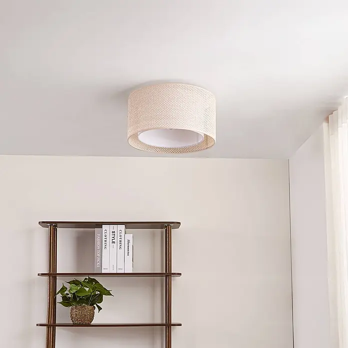 Lindby Deckenleuchte Soula - creme / amber, E27 - Helle beige gewebte Deckenleuchte mit Trommelschirm und weißem Innendiffusor, an einer Decke über einem Holzregal montiert.