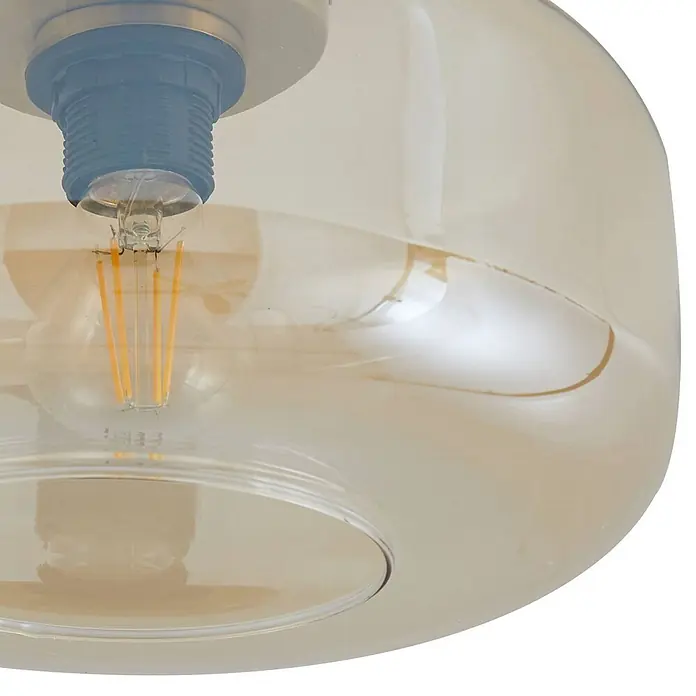 Lindby Deckenleuchte Hildur - creme / amber, E27 - Nahaufnahme einer LED-Glühfadenlampe in einem blauen Kunststoffsockel, umschlossen von einem bernsteinfarbenen Glasschirm.