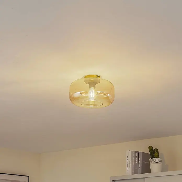 Lindby Deckenleuchte Hildur - creme / amber, E27 - Deckenleuchte aus bernsteinfarbenem Glas mit goldenem Metallsockel, beleuchtet einen Raum.
