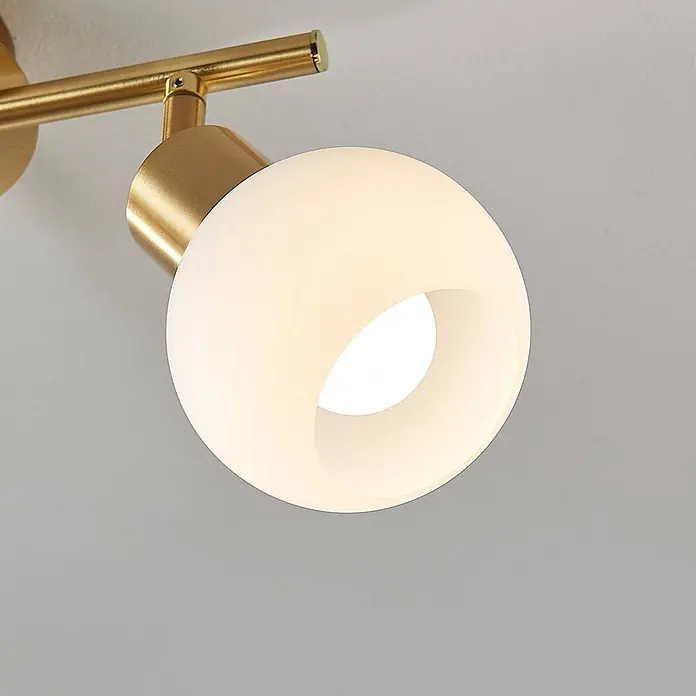 Lindby Deckenleuchte Elaina - messing / gold, E14 - Goldfarbener Messing-Strahler mit kugelförmigem weißem Opalglasschirm, leuchtende Glühbirne sichtbar.