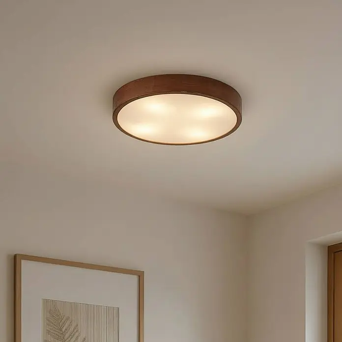 Lindby Deckenleuchte Tanju - Holz dunkel, E27 - Runde Deckenleuchte mit dunklem Holzrahmen und weißem, beleuchtetem Diffusor an einer cremefarbenen Decke.