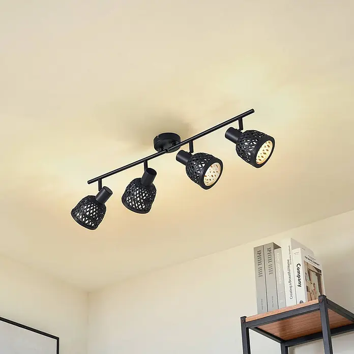 Lindby Deckenleuchte Eskil - schwarz, E14 - Moderne schwarze Metallschiene mit vier dekorativen Strahlern und gemusterten Schirmen an der Decke. Sie beleuchtet einen Bereich über einem Bücherregal.