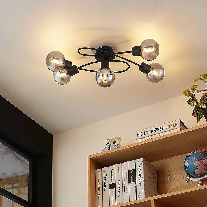 Lindby Deckenleuchte Elaina - schwarz, schwarz, E14 - Moderne schwarze Deckenleuchte aus Metall mit fünf rauchgrauen Kugellampen, beleuchtet einen Raum über einem Bücherregal.