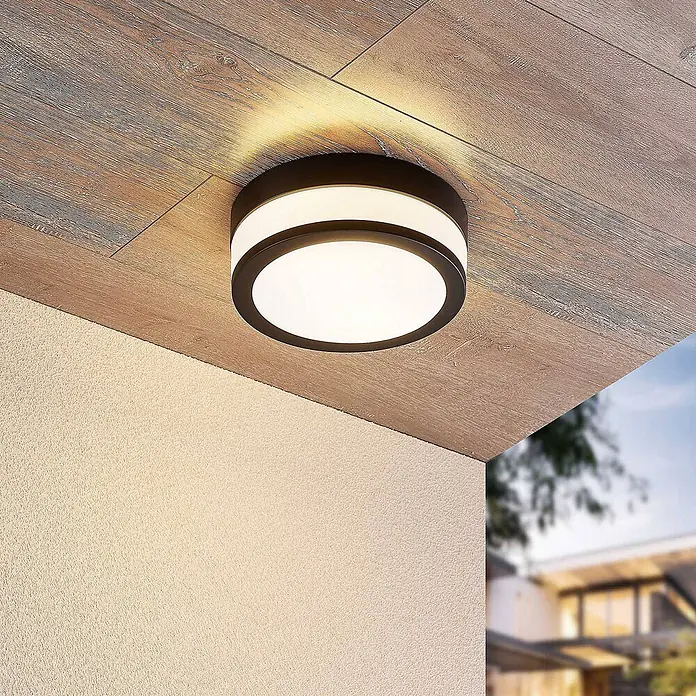 Lindby Deckenleuchte Flavi - schwarz, E27 - Runde, dunkel gerahmte Außen-Deckenleuchte mit weißem Diffusor, beleuchtet Holzdecke und Strukturwand.