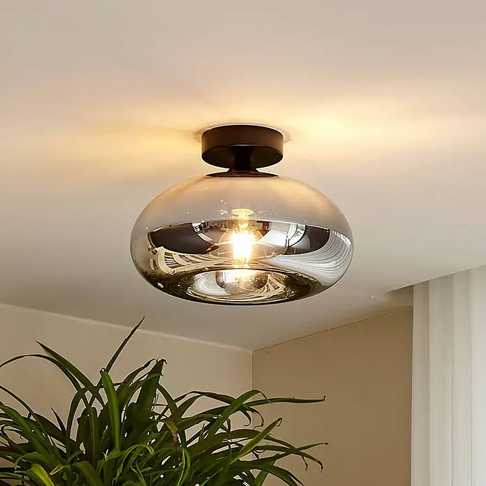 Lindby Deckenleuchte Zehra - schwarz, E27 - Eine moderne Deckenlampe mit Rauchglas-Kuppelschirm und dunklem Metallsockel, die warmes Licht wirft.