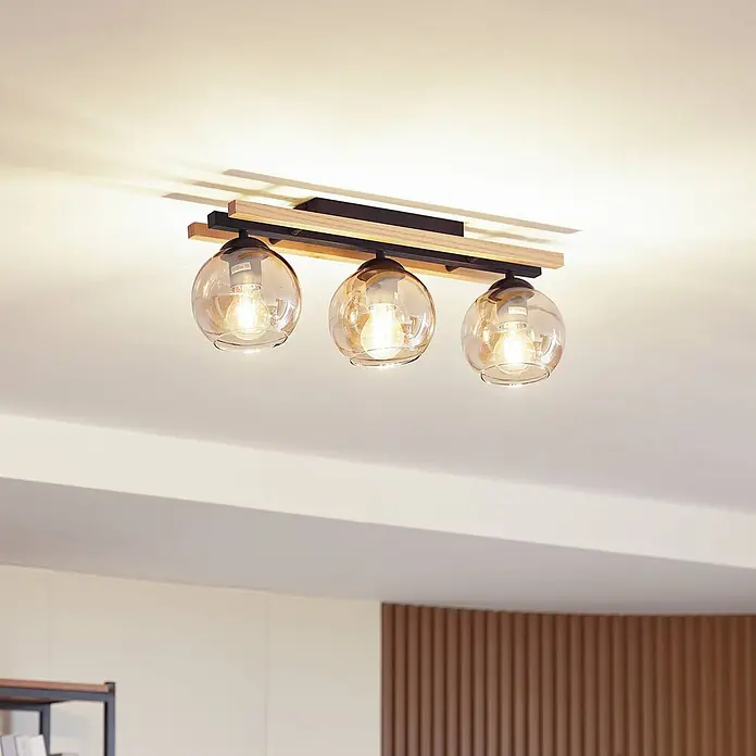 Lindby Deckenleuchte Enrique - schwarz, creme / amber, E27 - Deckenleuchte mit drei amberfarbenen Glaskugeln, schwarzem Metallrahmen und Holzapplikationen, an der Decke montiert.