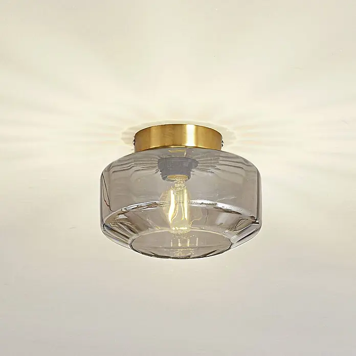 Lindby Deckenleuchte Hildur - L x B x H: 22 x 22 x 15,3 cm, alu / grau / zink, E27 - Deckenleuchte mit messingfarbener Basis und rauchgrauem Glasschirm, der eine Glühfadenlampe zeigt.