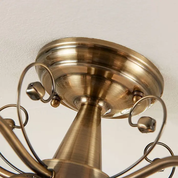 Lindby Deckenleuchte Corentin - bronze / altmessing, E14 - Nahaufnahme der dekorativen Halterung und des Mittelstiels einer Deckenleuchte in rustikalem Bronze-Finish, mit geschwungenen Verzierungen.