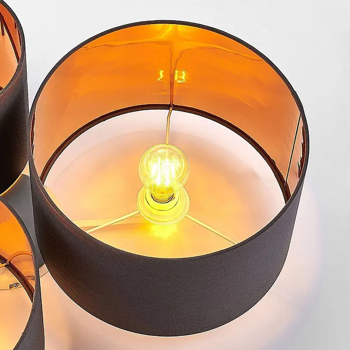 Lindby Deckenleuchte Laurenz - alu / grau / zink, E27 - Nahaufnahme eines Lampenschirms mit dunkelgrauer Stoffaußenseite und reflektierender orange-goldener Innenseite, mit brennender Glühbirne.