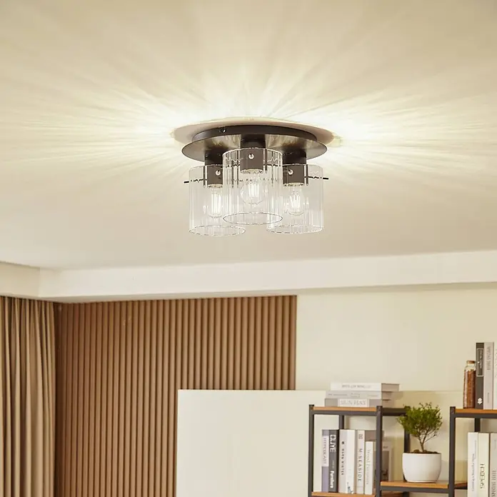 Lucande Deckenleuchte Eirian - L x B x H: 35 x 35 x 20 cm, schwarz, klar / transparent, E27 - Eine moderne Deckenleuchte mit dunklem Metallsockel und drei klaren gerippten Glasschirmen, die dekorative Lichtmuster wirft.
