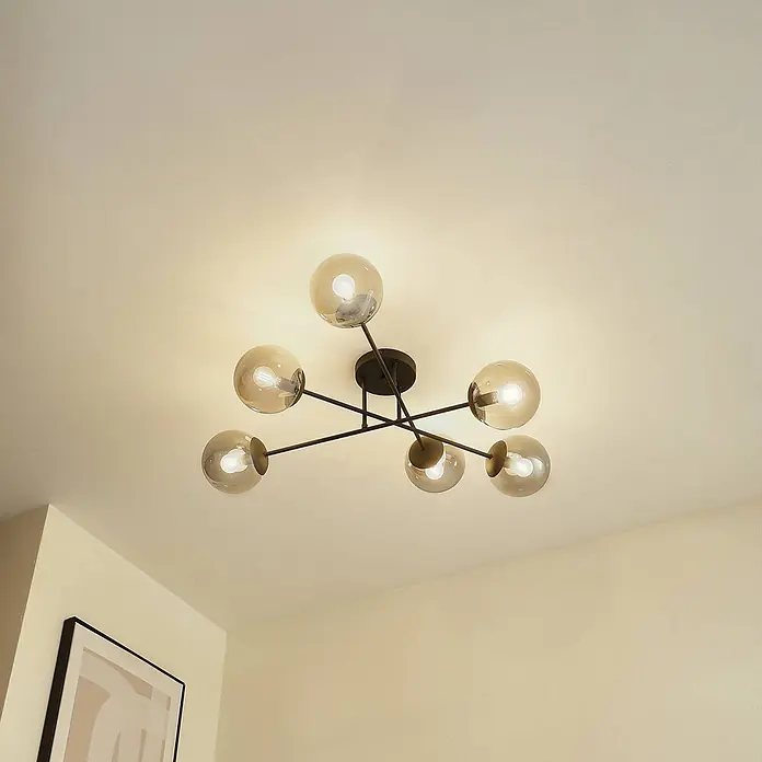 Lindby Deckenlampe in rauchgrau transparent, schwarz, Deckenleuchte -  - Eine moderne Deckenleuchte mit sechs bernsteinfarbenen Glaskugelschirmchen und schwarzen Metallarmen, die einen cremefarbenen Raum beleuchtet.