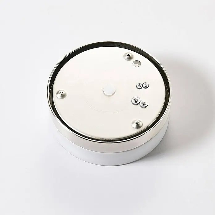 Lindby Deckenleuchte Amilia - L x B x H: 18 x 18 x 6,5 cm, alu / grau / zink, E27 - Kreisförmige weiße Basis mit einer metallisch-silbernen Deckplatte, versehen mit mehreren kleinen Schrauben, Löchern und einem zentralen weißen Knopf.