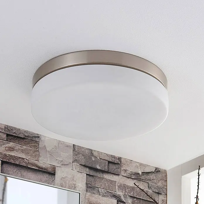 Lindby Deckenleuchte Amilia - L x B x H: 30 x 30 x 6,5 cm, alu / grau / zink, E27 - Runde Deckenleuchte mit gebürstetem Metallring und weißem Diffusor, an einer Decke über einer Steinwand montiert.