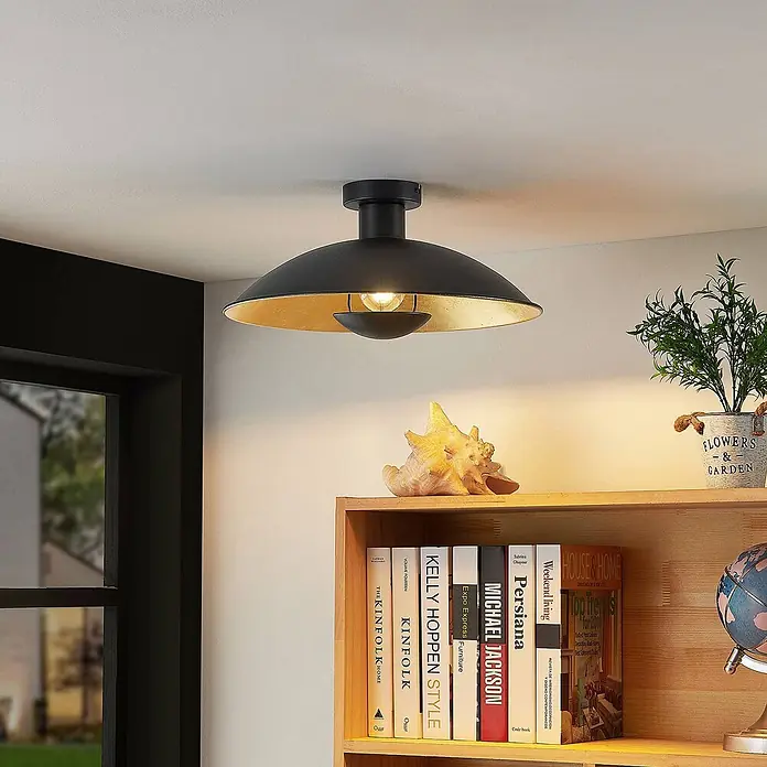 Lindby Deckenleuchte Narisara - L x B x H: 40 x 40 x 19 cm, schwarz, schwarz, E27 - Schwarze Deckenleuchte mit goldenem Inneren beleuchtet einen Raum über einem Bücherregal.