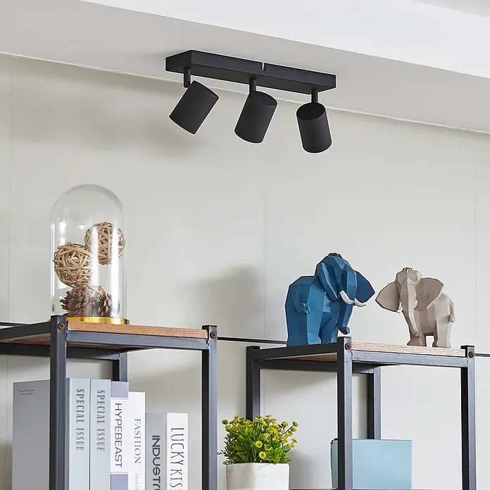 Lindby Deckenstrahler Jorell - L x B x H: 35 x 8 x 13 cm, schwarz, schwarz, GU10 - Schwarze Deckenleuchte mit drei Strahlern, beleuchtet ein Regal darunter.