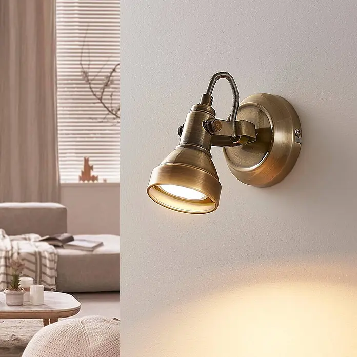 Lindby Deckenstrahler Perseas - bronze / altmessing, bronze / altmessing, GU10 - Verstellbarer Wandstrahler aus Altmessing, der ein warmes Licht an eine Wand in einem gemütlichen Raum wirft.