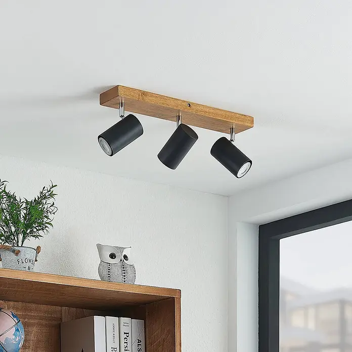 Lindby Deckenstrahler Maniva - Holz hell, schwarz, GU10 - Deckenleuchte aus Holz mit drei schwarzen zylindrischen Strahlern, an der Decke montiert.