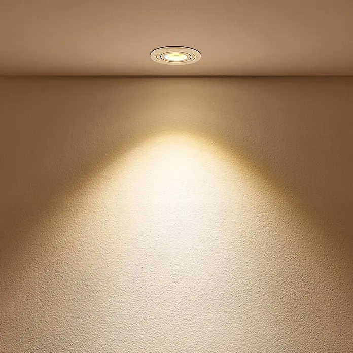 Arcchio Deckenstrahler Sophia - weiß / opal, weiß / opal, GU10 - Ein weißer Einbaustrahler spendet warmes Licht auf eine strukturierte beige Wand und beleuchtet den Bereich darunter.