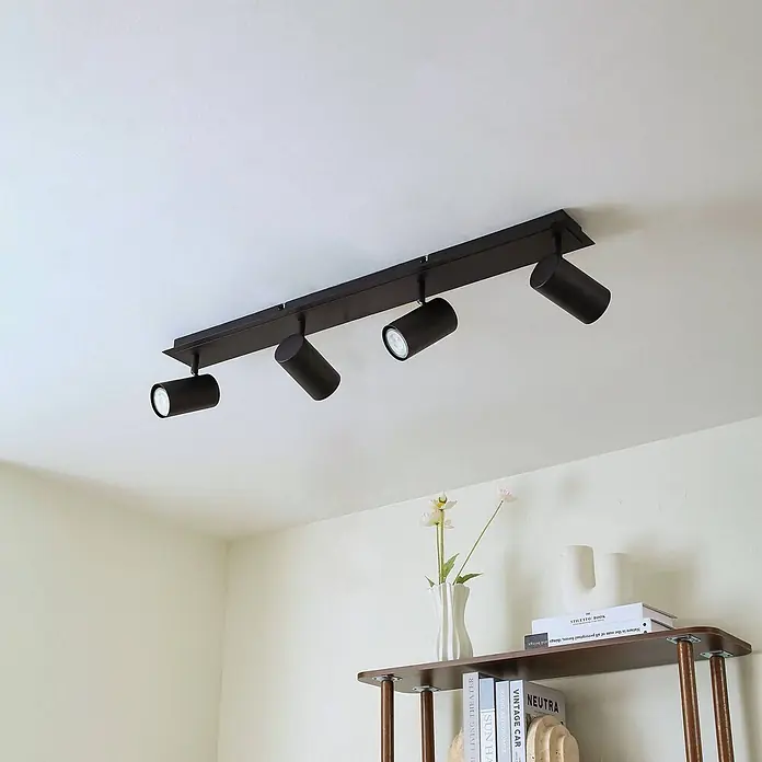 Lindby Deckenstrahler Joffrey - schwarz, schwarz, GU10 - Schwarze Deckenleuchte mit vier verstellbaren Strahlern, an weißer Decke über einem Regal montiert.